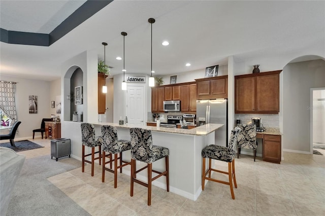 kitchen featuring a breakfast bar, brown cabinetry, decorative backsplash, stainless steel appliances, and arched walkways