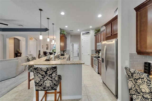 kitchen featuring light stone counters, open floor plan, a peninsula, a kitchen bar, and stainless steel appliances