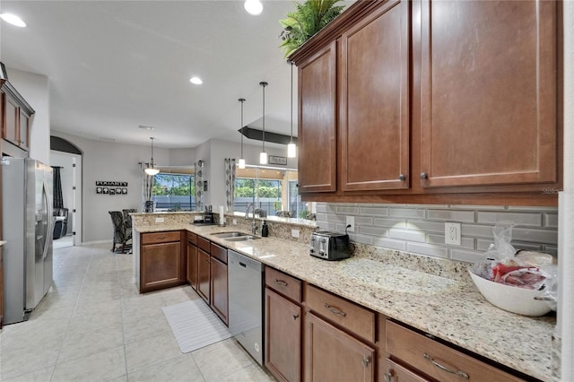 kitchen with light stone countertops, a peninsula, a sink, stainless steel appliances, and backsplash