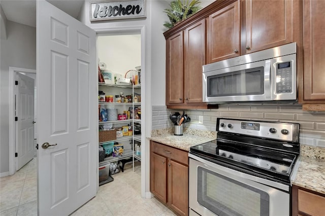 kitchen featuring backsplash, light tile patterned flooring, light stone counters, and stainless steel appliances