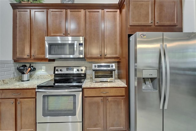 kitchen featuring decorative backsplash, appliances with stainless steel finishes, a toaster, and light stone counters