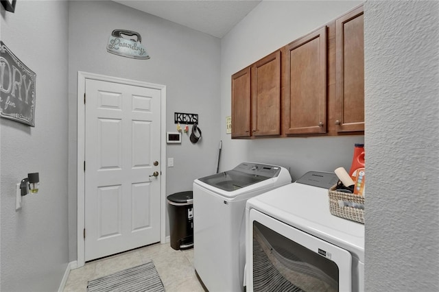 washroom featuring cabinet space, washer and clothes dryer, light tile patterned flooring, and baseboards