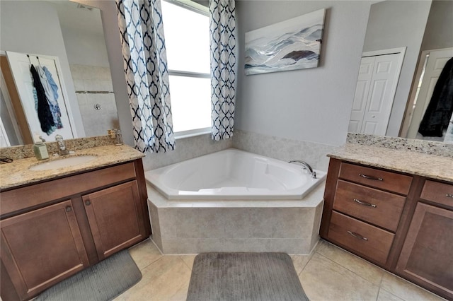 full bath with tile patterned floors, a garden tub, two vanities, and a sink