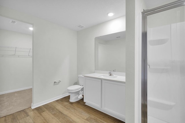 bathroom featuring vanity, hardwood / wood-style flooring, a shower stall, a walk in closet, and baseboards