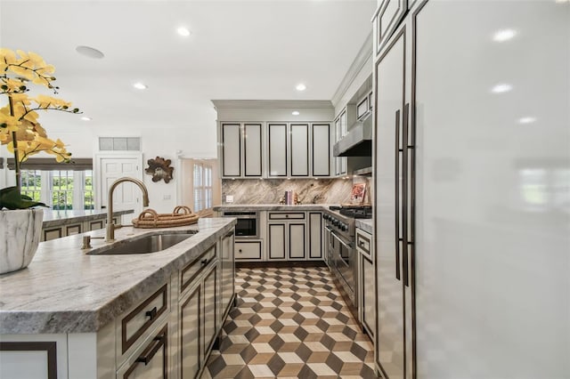 3313 W Mullen Ave, Tampa, FL 33609 - kitchen with under cabinet range hood, backsplash, a center island with sink, a sink, and appliances with stainless steel finishes