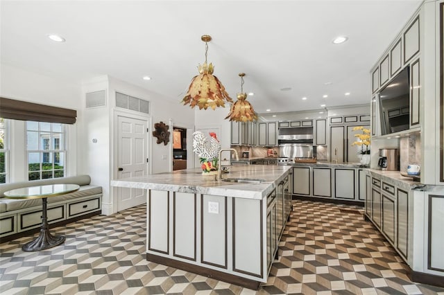 3313 W Mullen Ave, Tampa, FL 33609 - kitchen featuring decorative backsplash, a kitchen island with sink, under cabinet range hood, a sink, and gray cabinetry