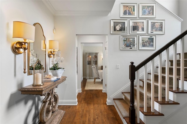 foyer entrance with dark wood-type flooring, ornamental molding, baseboards, and stairs