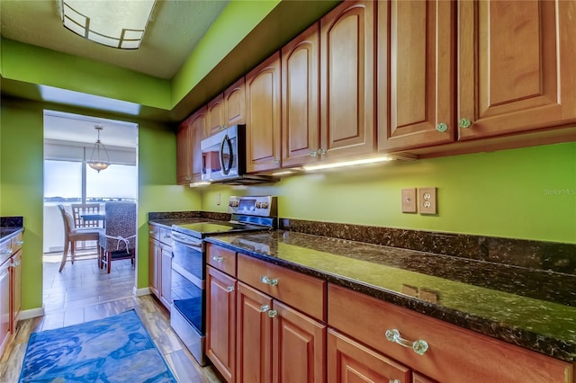 80 Rogers St Unit 2A, Clearwater, FL 33756 - kitchen featuring light wood finished floors, hanging light fixtures, brown cabinets, dark stone countertops, and stainless steel appliances