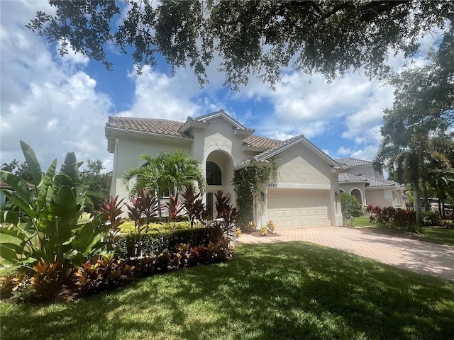 mediterranean / spanish house with a tiled roof, a garage, stucco siding, a front lawn, and driveway