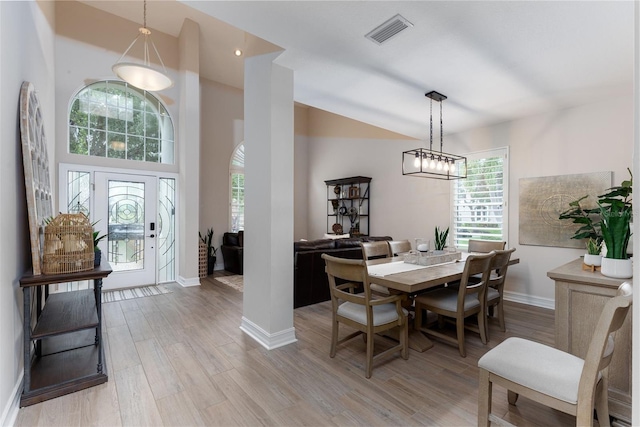 dining area with high vaulted ceiling, visible vents, baseboards, light wood-style floors, and an inviting chandelier