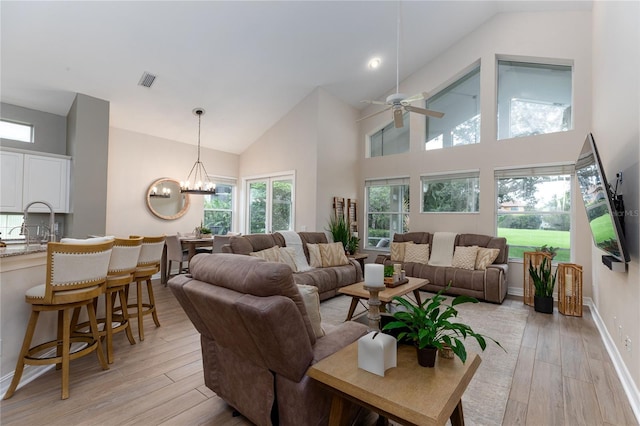 living room featuring high vaulted ceiling, visible vents, ceiling fan with notable chandelier, and light wood finished floors