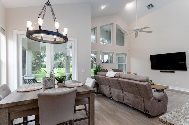 dining space with ceiling fan with notable chandelier, a healthy amount of sunlight, light wood finished floors, and visible vents