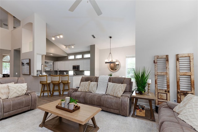 living area featuring rail lighting, light wood-type flooring, high vaulted ceiling, ceiling fan with notable chandelier, and visible vents