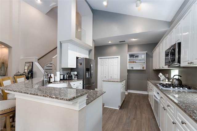 kitchen with a kitchen island, a sink, dark wood-style floors, a peninsula, and appliances with stainless steel finishes