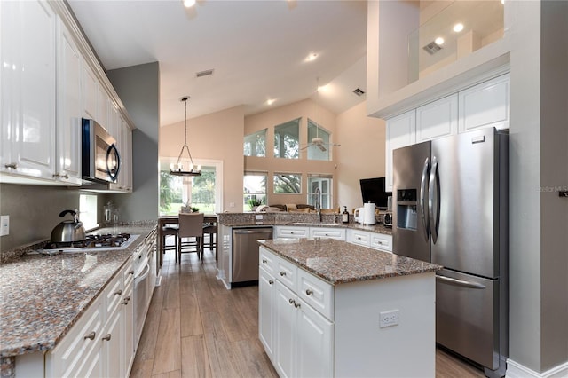 kitchen with a sink, appliances with stainless steel finishes, a peninsula, a center island, and light wood-style floors