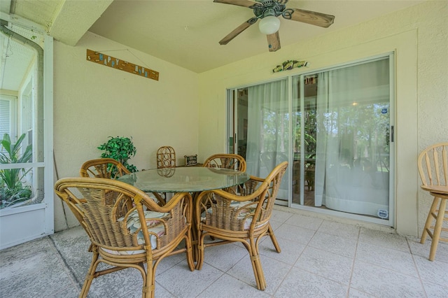 sunroom with ceiling fan, a textured wall, outdoor dining area, and lofted ceiling