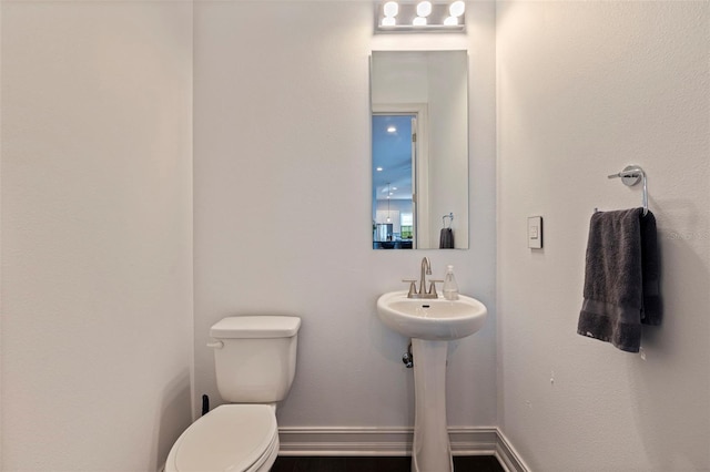 half bath featuring baseboards, toilet, and a sink