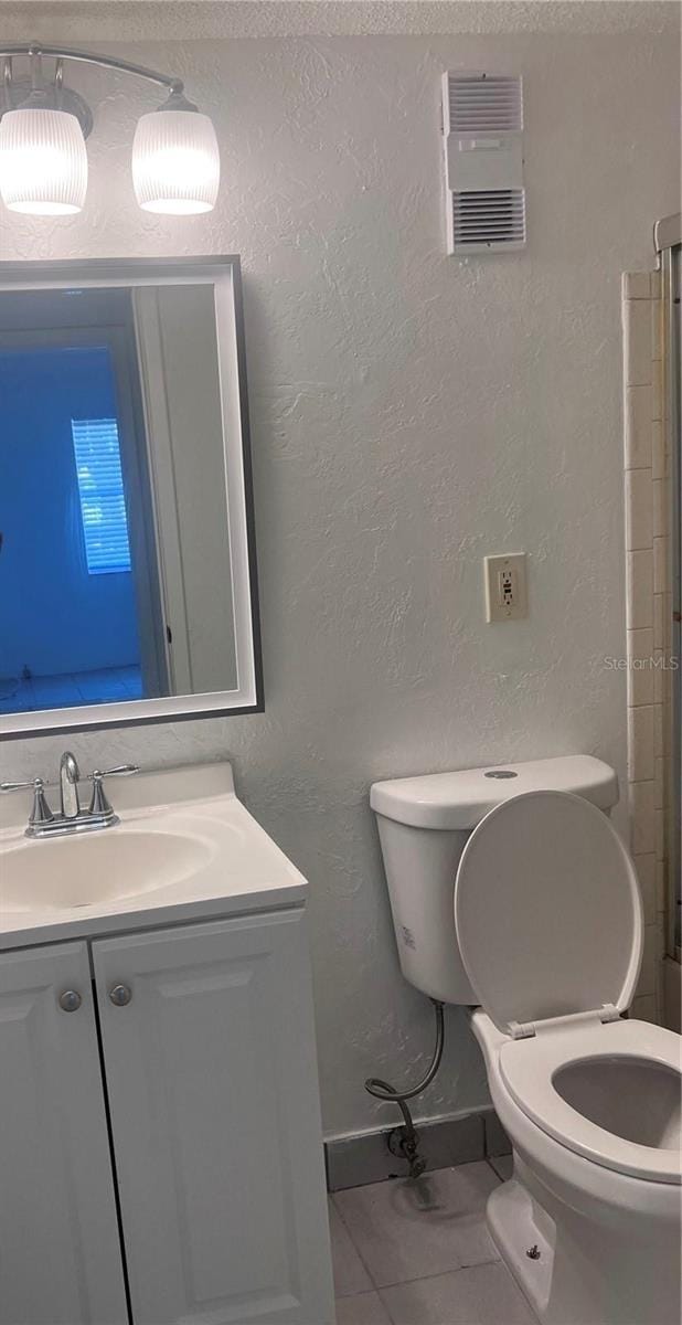 bathroom featuring vanity, visible vents, toilet, tile patterned floors, and a textured wall