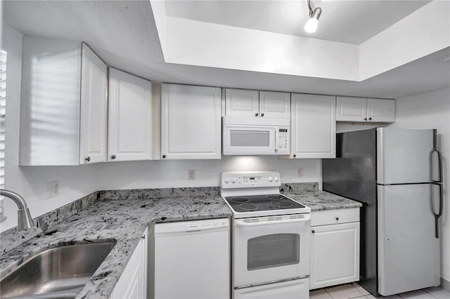 kitchen with white cabinets, light stone counters, a sink, and white appliances