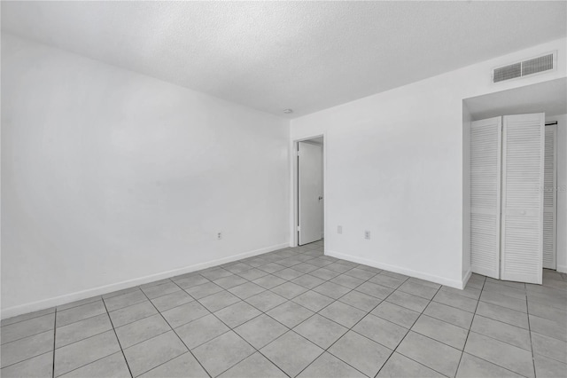 empty room featuring baseboards, visible vents, a textured ceiling, and light tile patterned floors