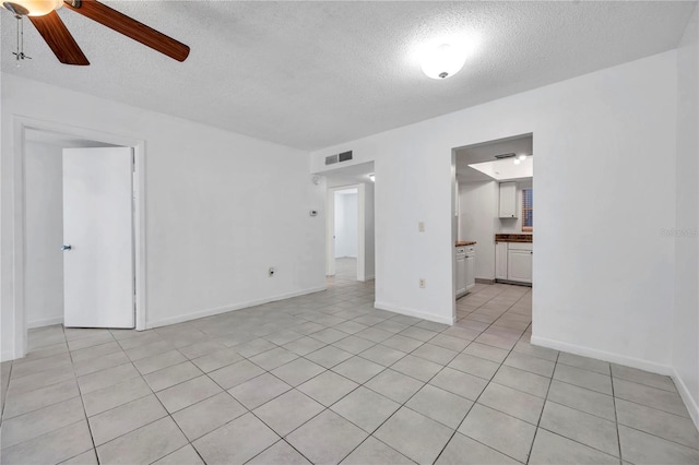 interior space with a ceiling fan, a textured ceiling, light tile patterned floors, baseboards, and visible vents