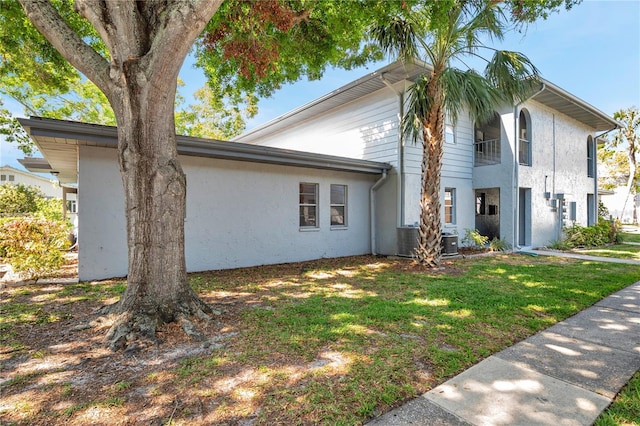 view of side of home with central AC, a lawn, a balcony, and stucco siding