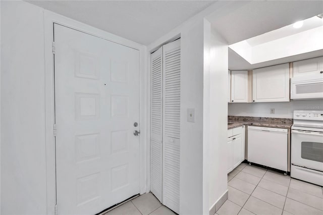 kitchen with light tile patterned flooring, baseboards, white cabinetry, and white appliances
