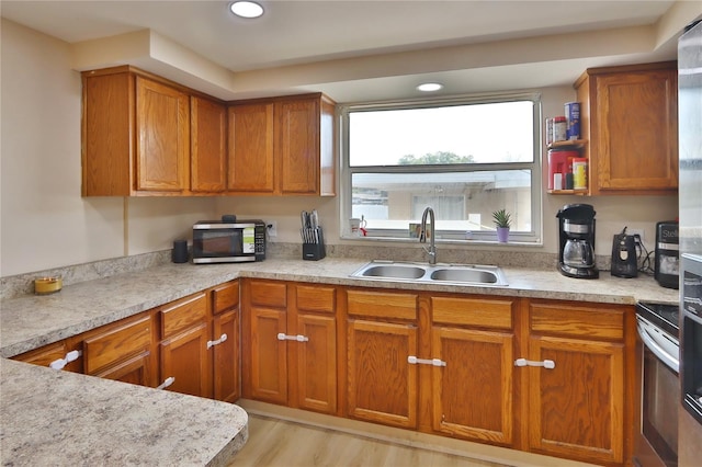 kitchen featuring light countertops, brown cabinets, stainless steel electric range, a sink, and light wood-type flooring