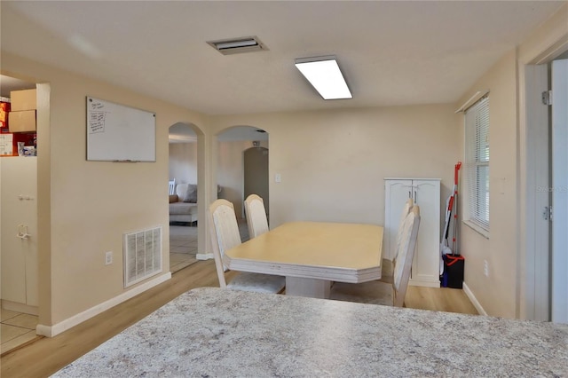 dining space with baseboards, visible vents, wood finished floors, and arched walkways