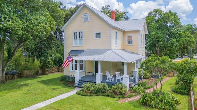 view of front of home with a chimney, fence, a front lawn, metal roof, and a porch