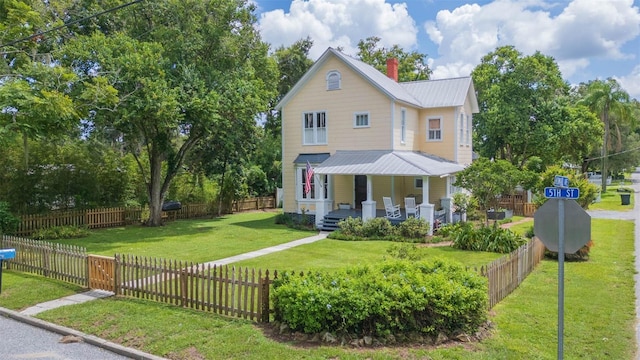 view of front of property with metal roof, a chimney, a fenced front yard, a front lawn, and a porch