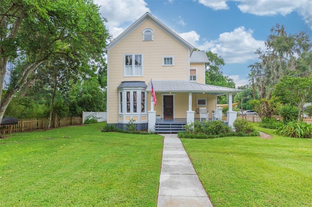 view of front of property featuring covered porch, fence, metal roof, and a front yard