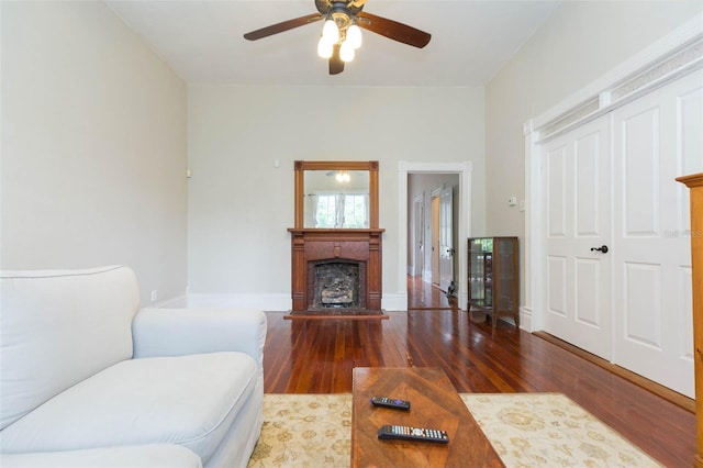 living area with baseboards, wood finished floors, a fireplace with raised hearth, and a ceiling fan