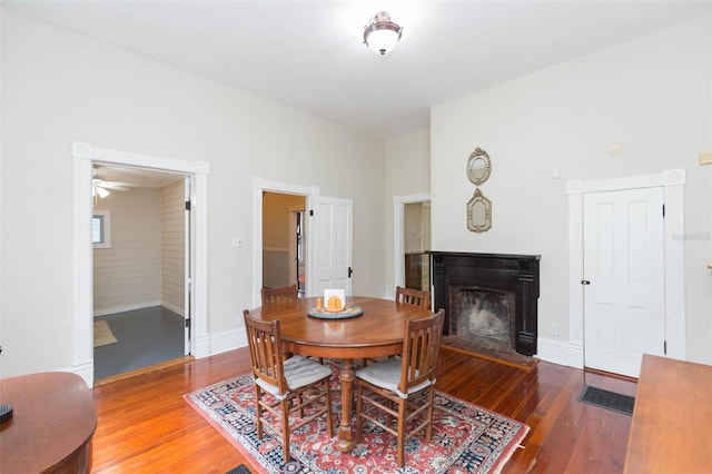 dining space with a fireplace with flush hearth, baseboards, a ceiling fan, and wood-type flooring