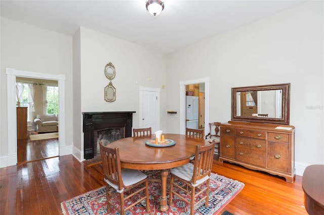 dining area with baseboards, a fireplace, a high ceiling, and light wood-style floors