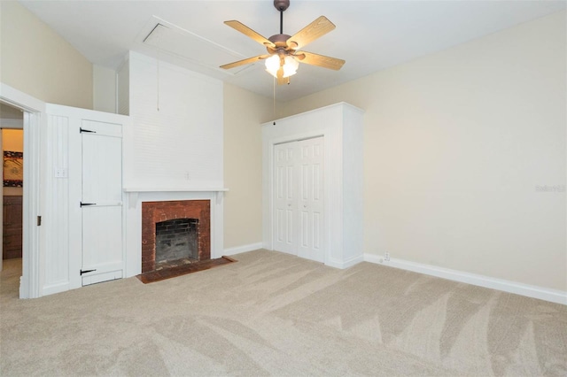 unfurnished living room featuring a ceiling fan, attic access, a fireplace with flush hearth, baseboards, and carpet