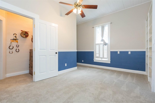 unfurnished room featuring a wainscoted wall, baseboards, carpet flooring, and a ceiling fan