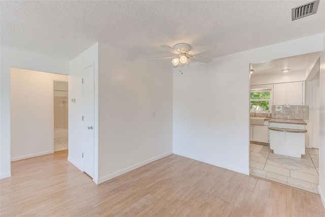 spare room with a textured ceiling, a ceiling fan, visible vents, and light wood-type flooring