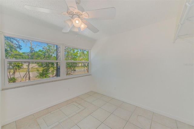 empty room with baseboards, a textured ceiling, light tile patterned flooring, and a ceiling fan