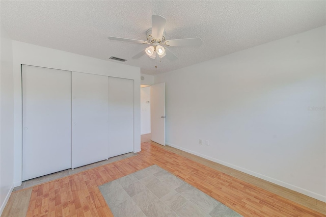unfurnished bedroom featuring a closet, a textured ceiling, visible vents, and light wood-style floors