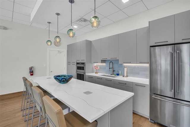 kitchen with a kitchen island, tasteful backsplash, gray cabinetry, a sink, and stainless steel appliances