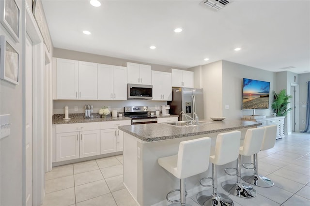 kitchen with an island with sink, white cabinets, visible vents, stainless steel appliances, and a sink