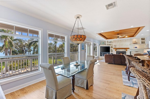 450 Bayshore Dr, Terra Ceia, FL 34250 - dining room with light wood-style flooring, visible vents, ornamental molding, a lit fireplace, and a tray ceiling