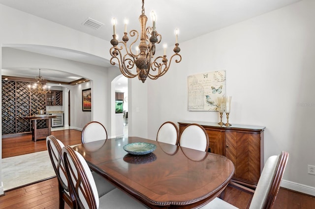 dining room with visible vents, wood finished floors, arched walkways, and a chandelier