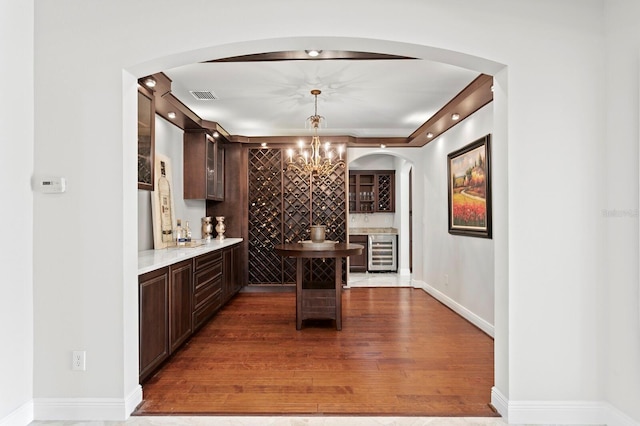 wine cellar with arched walkways, visible vents, wood finished floors, and beverage cooler