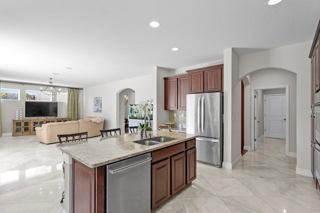 kitchen featuring light stone counters, a sink, stainless steel appliances, marble finish floor, and arched walkways