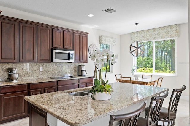 kitchen featuring light stone countertops, stainless steel microwave, a center island with sink, tasteful backsplash, and a breakfast bar area