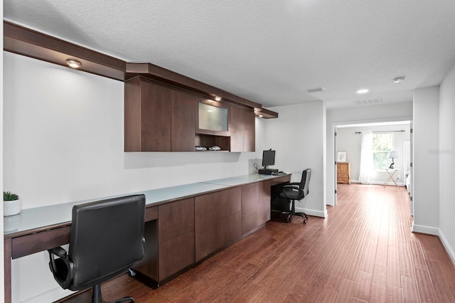 home office featuring a textured ceiling, visible vents, baseboards, built in study area, and dark wood-style floors