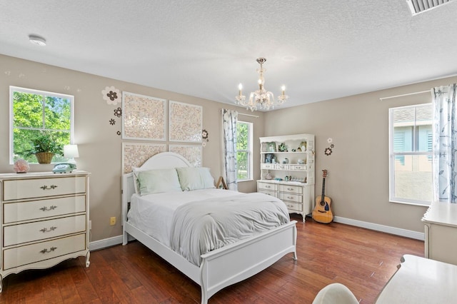 bedroom with a chandelier, wood-type flooring, a textured ceiling, baseboards, and visible vents