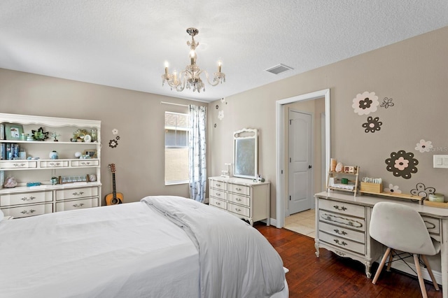 bedroom featuring an inviting chandelier, wood finished floors, a textured ceiling, and visible vents